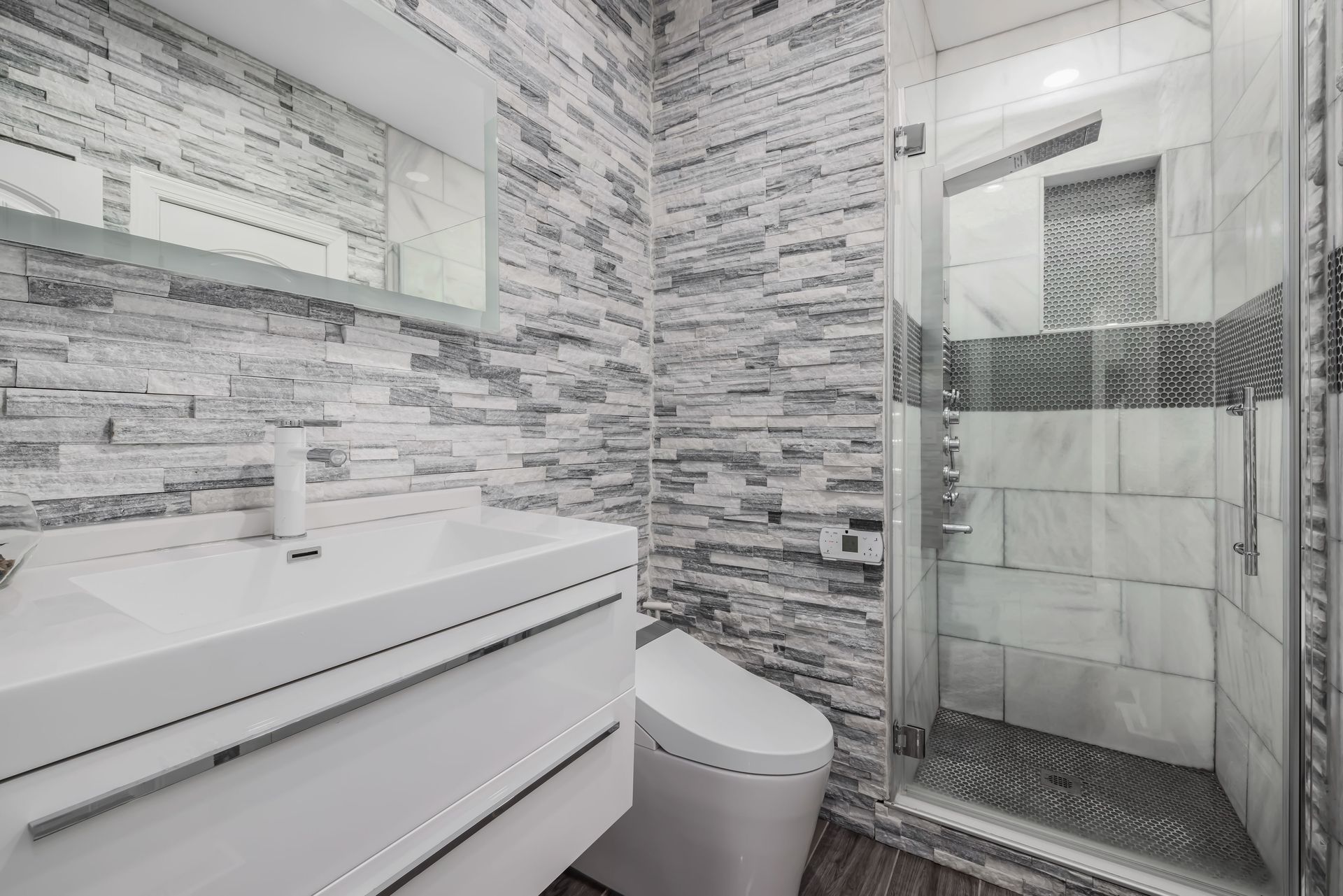 Stylish modern bathroom featuring a glass shower, stone walls, and sleek white vanity.